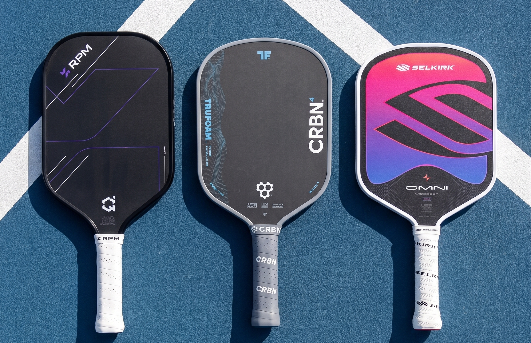 Three pickleball paddles laid out side by side on a blue Hong Kong court — an elongated RPM Q2, a hybrid CRBN4 TruFoam Waves, and a widebody Selkirk Omni.