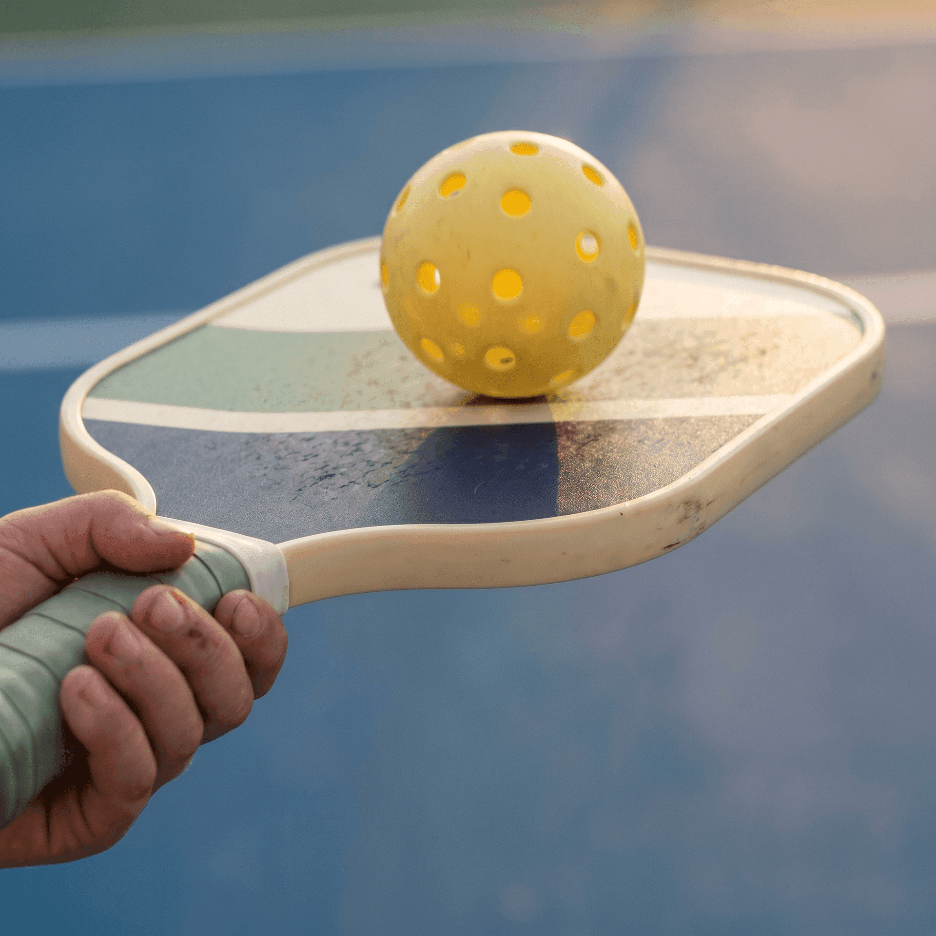 Child's hand gripping a junior pickleball paddle with a yellow ball