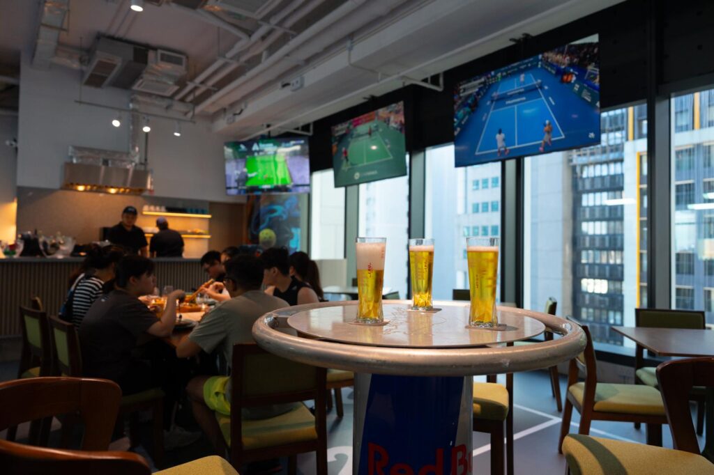 Beers on a table at the Courtside Café & Bar with match TVs overhead and floor-to-ceiling windows