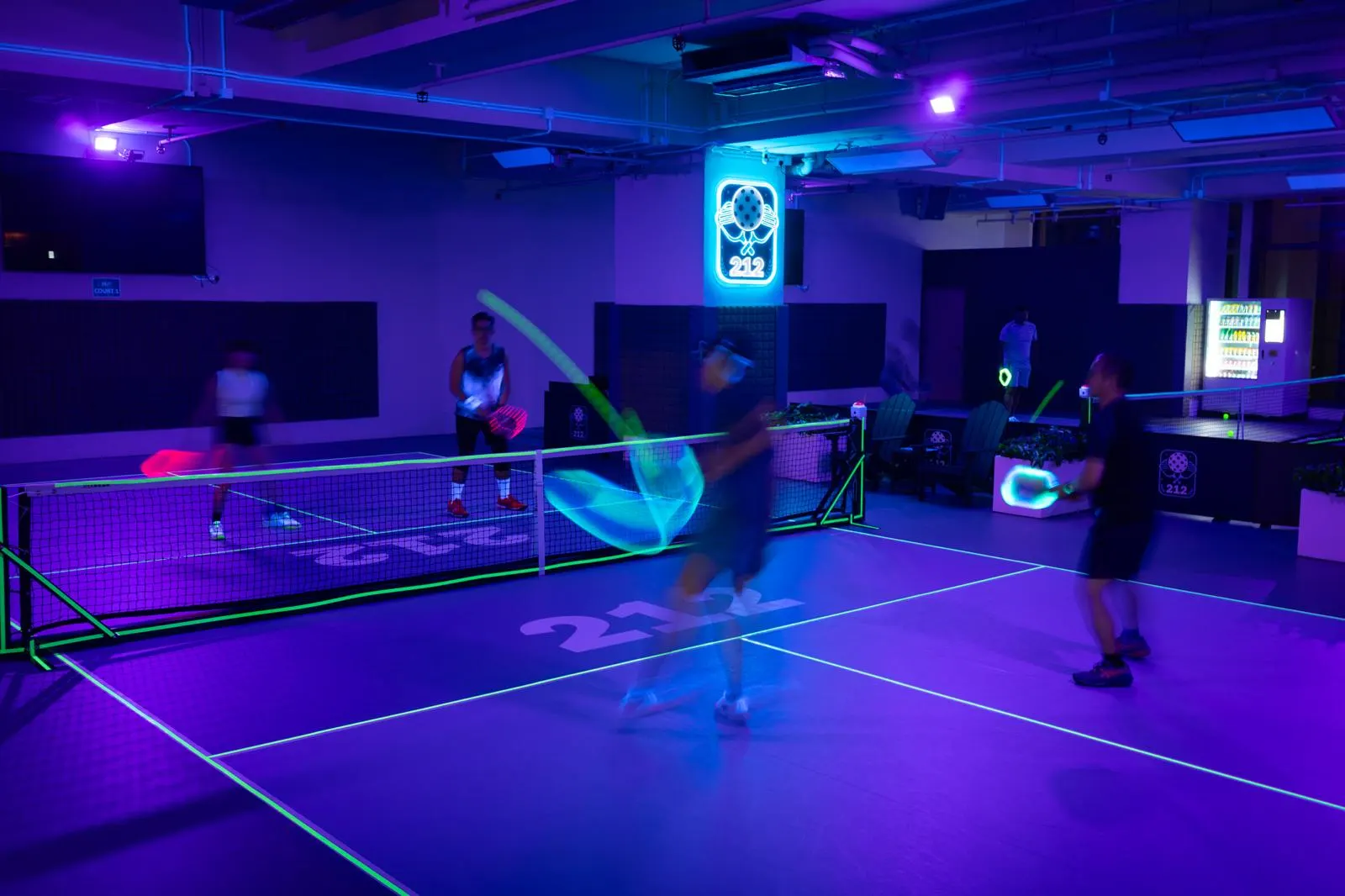 Players mid-rally under UV blacklights with glowing paddles and neon court lines at 212HK After Dark