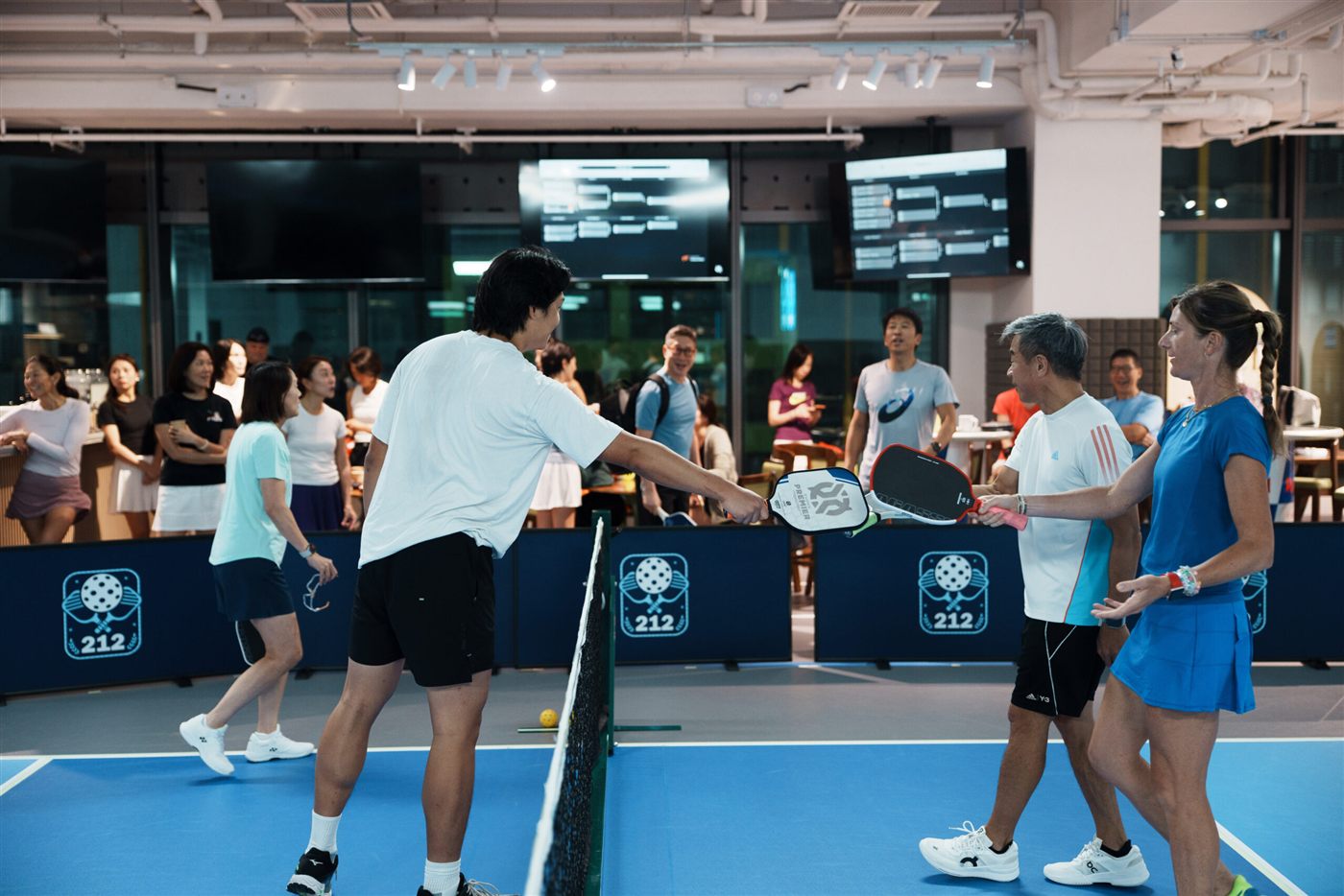 Players tapping paddles at the net during an open play night at 212HK
